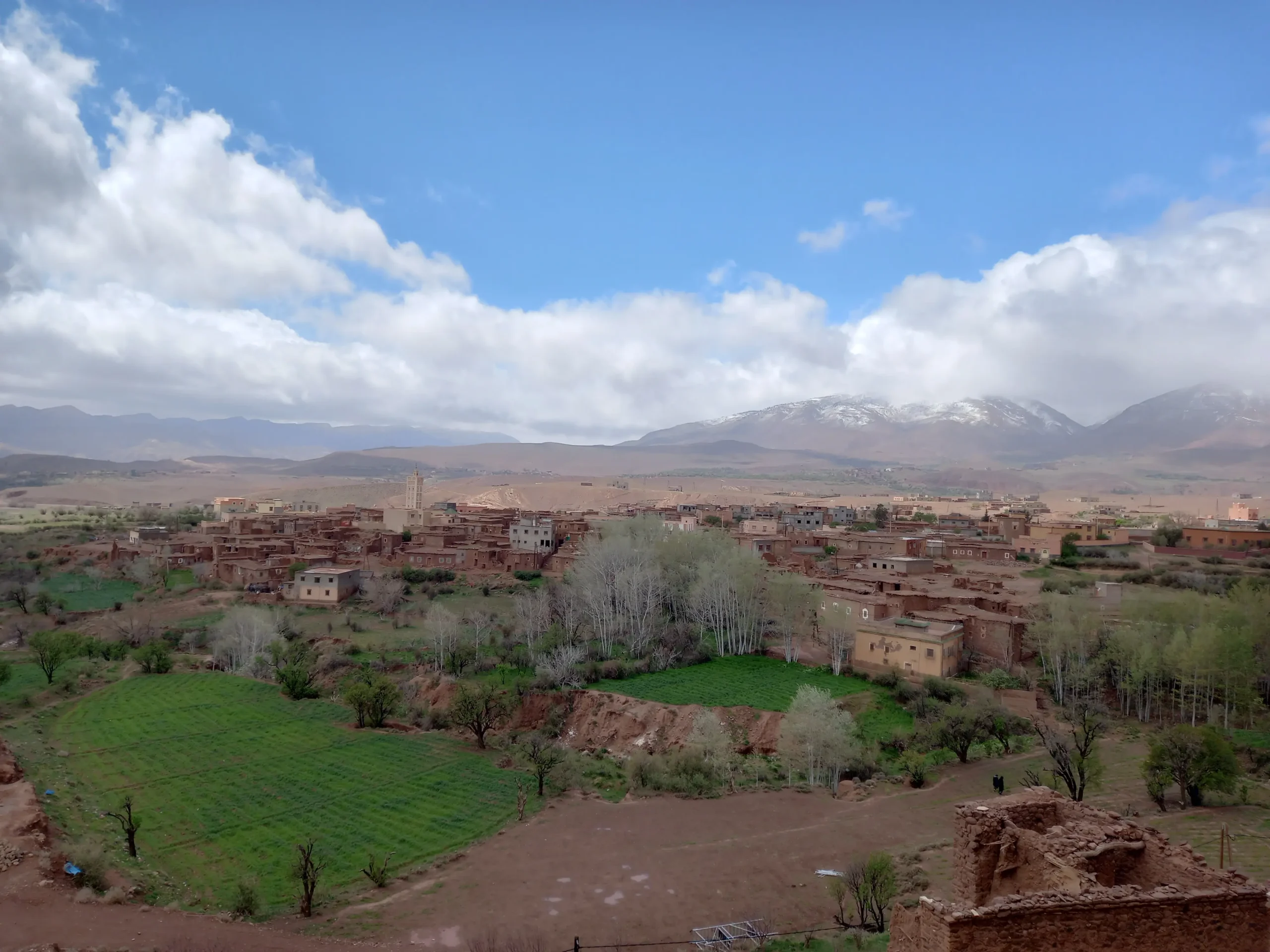 Traditional Berber village with green fields and Atlas Mountains in the background — a stunning travel destination in Morocco.