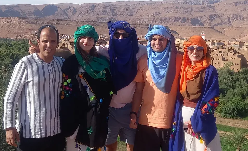 American tourists in Berber clothes with our English-speaking tour driver, green valley and adobe houses in the background